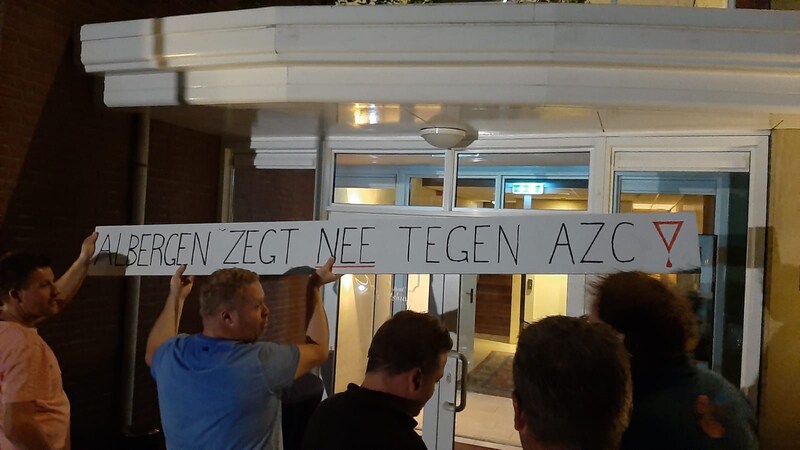 Een groep boze mensen hangt een protestbord op aan de gevel van de ingang van Landhotel ’t Elshuys.